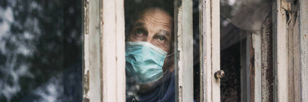 istock Lonely older man wearing medical face mask looking through window. 1327938114