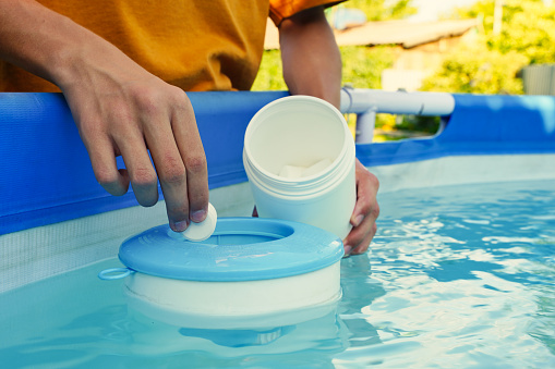 Hand holding white chlorine tablets over swimming pool skimmer. Chlorination of water in pool for disinfection and prevention against the development of microbes. High quality photo