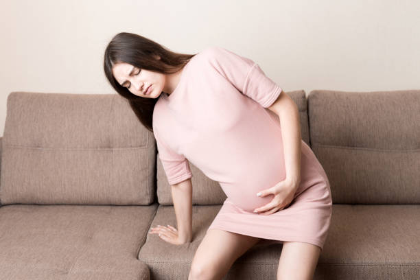istock Pregnant Lady Having Massaging Lower belly Sitting On Sofa Indoor. Pregnancy Problems Concept. Maternity healthcare 1327945927