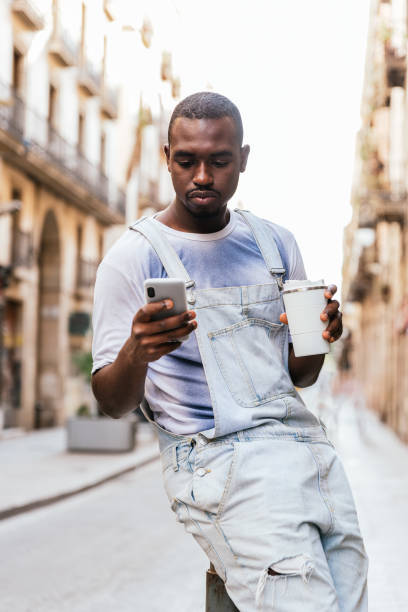 彼の携帯電話を使用して街で待っているアフロアメリカの若者の垂直肖像画 - single line urban scene outdoors vertical ストックフォトと画像