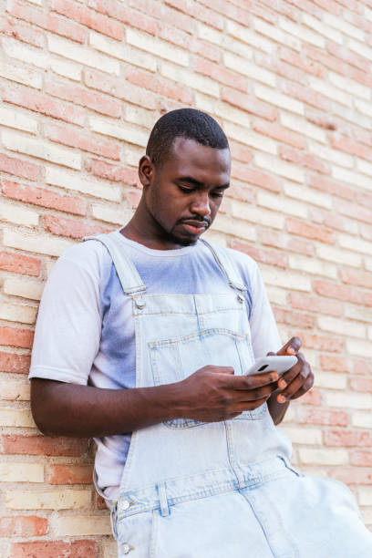 istock young african man leaning on a brick wall and using his smart phone 1327948801