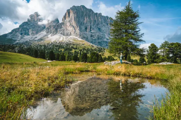 Woman hiking in Val Gardena. Pond and reflection of Sassolungo Langkofel mountain. Dolomites, Italy.