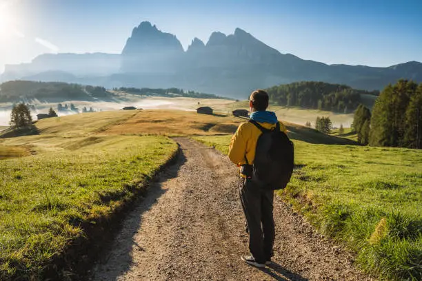 Man hiker on the road admire sunrise at Alpe di Siusi, Dolomites mountains, Italy.