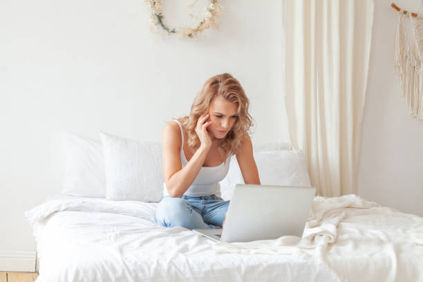 istock Blonde woman sitting on sofa relaxing while browsing online shopping website. Female model browsing through the internet during free time at home. 1327954591