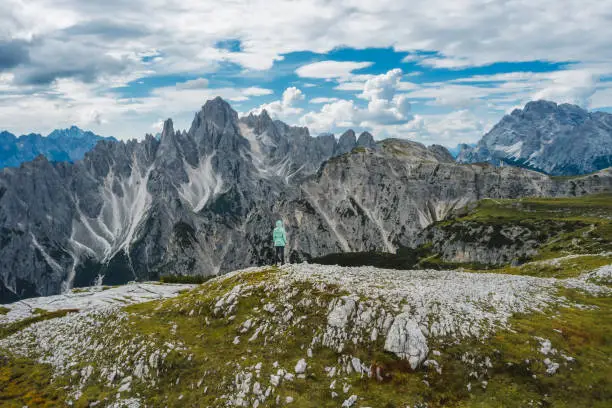 Aerial view of a woman hiker in green jacket against Cadini di Misurina mountain peaks in background. Italian Alps, Dolomites, Italy, Europe.