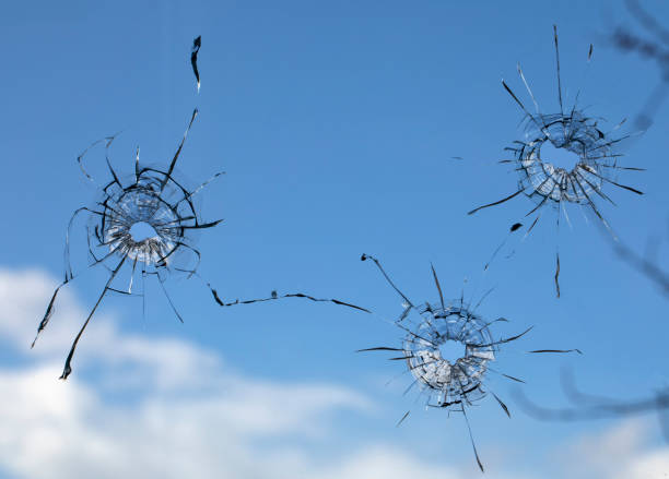 istock holes and cracks from bullets in glass, on sky background 1327958179