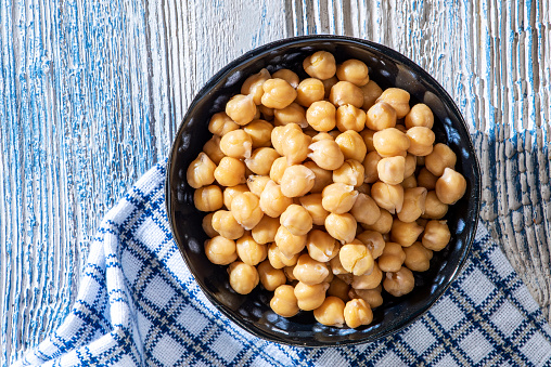 Boiled chickpeas in bowl on blue wooden background and tablecloth.