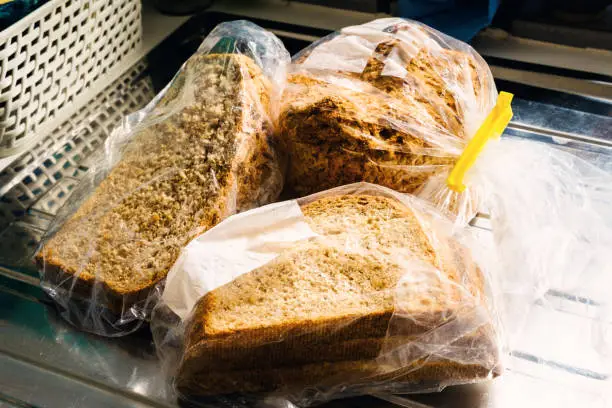 Three bags of bread defrosting on a kitchen counter draining board.