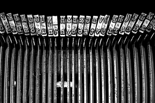 Detail of the typebars of an antique typewriter. Metal parts with alphabet letter moulds. Black and white background image useful for creative concepts, writing, referring to the past.