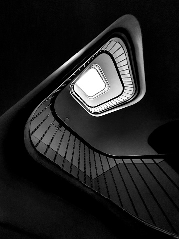 Black and white abstract background image. Perspective view of the interior of a building. Useful image for concepts of success, reaching a goal, reaching the top. It shows between light and shadow the path to follow to achieve a goal.