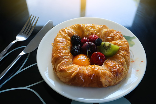 Danish pastry with remix fruits on the white plate in the morning background. Dark tone.