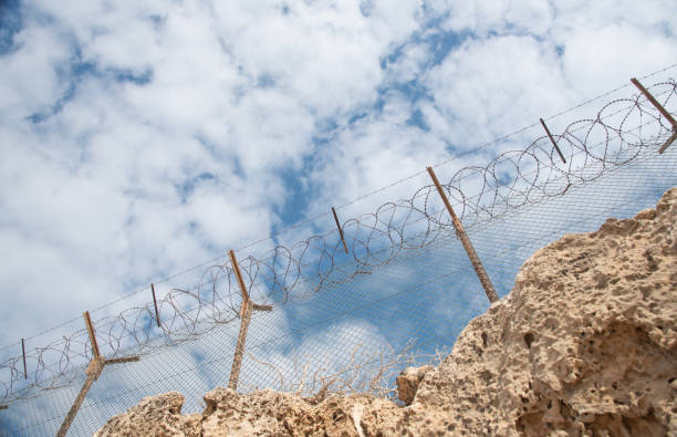 istock Security fence with barbed wire against a blue cloudy sky 1327963340