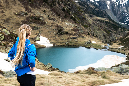 Rear view of young beautiful woman standing and looking at Tristaina lake view in Pyrenees mountains, Andorra.