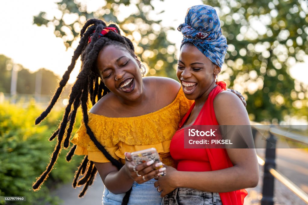 Two female friends with smartphone, smiling outdoors Friendship Stock Photo