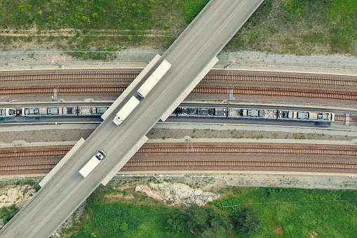 Two trucks crossing a bridge over a railway with a train.