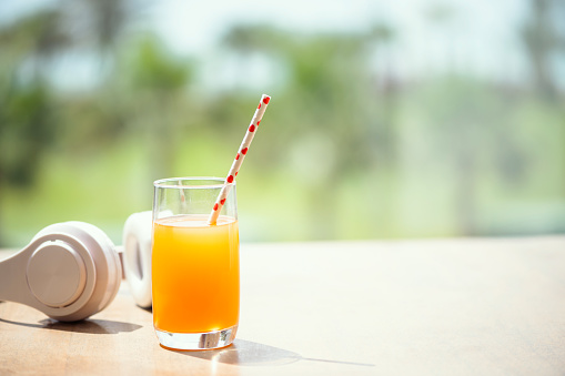 Headphones, orange juice on the table in the palm tree forest. Summer vocation. Copy space. Concept