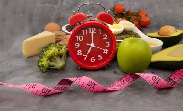 Photo of Intermittent fasting with Red  alarm clock for diet plan as a healthy food and measuring  tape image