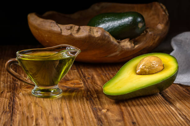 half avocado fruit and avocado oil in a glass bowl on old rustic table. healthy eating, diet, body care and hair care concept. - avocado oil bildbanksfoton och bilder