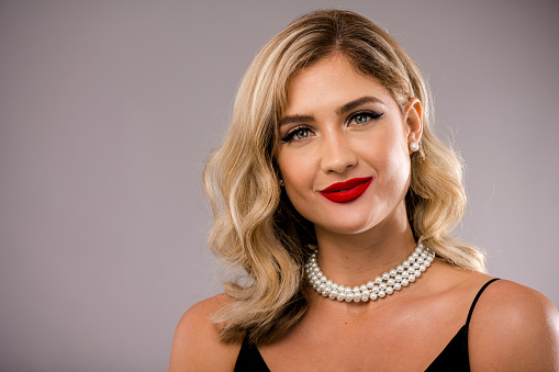 Headshot of a glamorous young woman wearing pearls and red lipstick