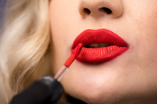 Macro shot woman applying bright red lipstick