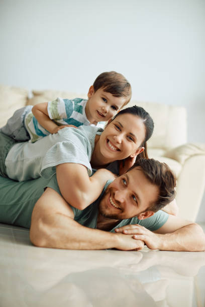 famiglia felice che fa piramide umana sul pavimento di casa e guarda la macchina fotografica. - floor two parent family couple home interior foto e immagini stock