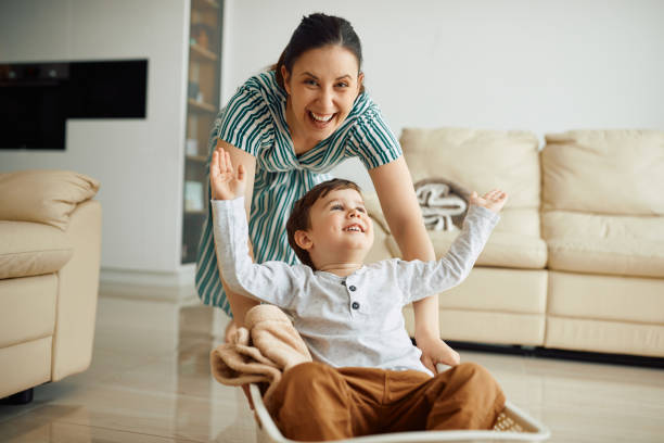 istock Happy mother pushing her small son in a laundry basket while playing together at home. 1327985771