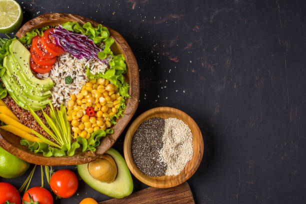 istock Buddha bowl with chickpea, avocado, wild rice, quinoa seeds, bell pepper, tomatoes, greens, cabbage, lettuce on shabby dark stone table and wooden bowl with chia and sesame seeds. Top view. 1327988302