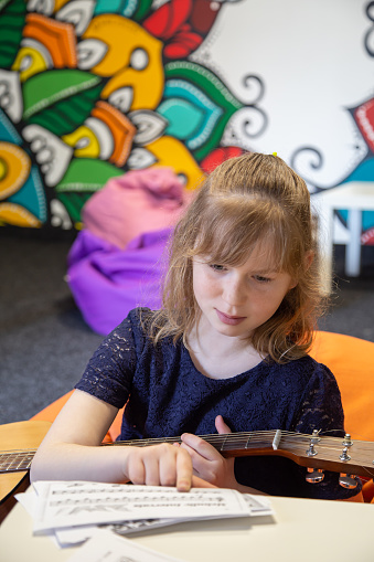 A little girl with a guitar learns solfeggio, sheet music and music theory.
