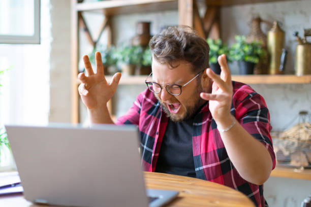 Young man yells at the laptop monitor. He's got a big problem stock photo