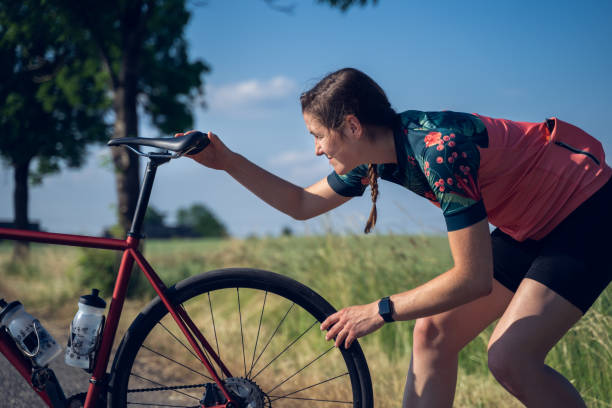 若い女性のサイクリストのクローズアップは、田舎道でサイクリングセッションを開始する前に、彼女のレーシングバイクの座席をチェックします。 - 鞍 ストックフォトと画像