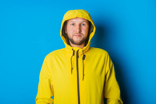 istock Young man in a yellow jacket in a hood on a blue background 1328001469