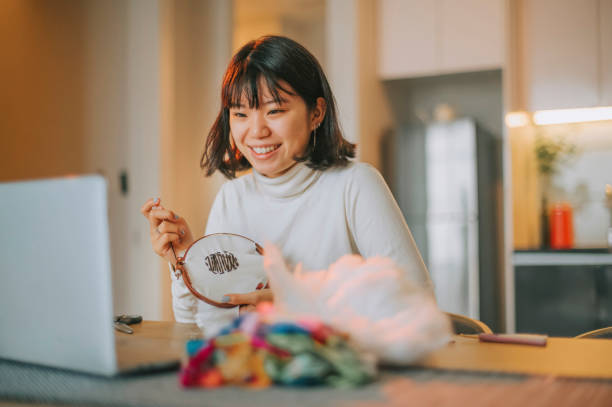 adolescente chinoise asiatique broderie point de croix artisanat pendant la soirée apprendre d’internet avec ordinateur portable à la maison côté agitation - embroidery cross stitch needle sewing photos et images de collection