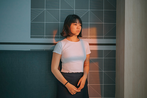 portrait asian chinese teenage girl standing in front of bedroom wall with sunset light on face from window