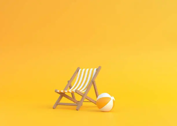 Photo of Striped deck chair and beach ball on a yellow background
