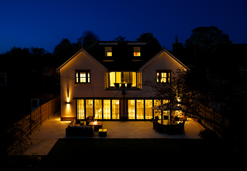 a view over a luxury new home taken from an elevated position (telescopic mast) during the evening so as to catch the indigo blue evening sky. All of the light of the house have been switched on and the garden fireplace as well.