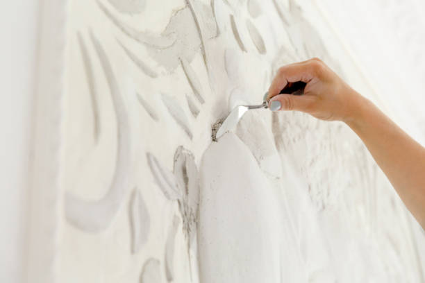 female worker puts putty mortar on a wall with a bas-relief
