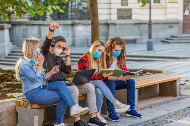 istock Beautiful Students are Working on a Laptop in Public Park with Preventive Measures due to Coronavirus. 1328018897