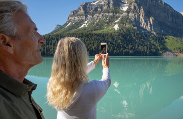 coppia escursionistica matura scatta foto di lake louise al cellulare - hiking mature adult women senior adult foto e immagini stock