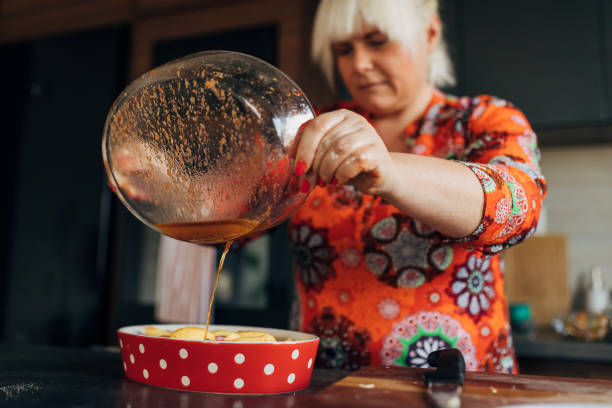 Healthy woman, pouring her special sauce into the baking pot with raw vegetables while preparing her vegan meal