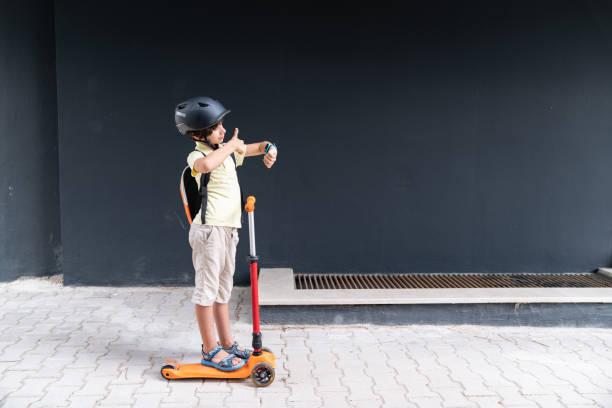 istock Photo Of Elementary Schoolboy Using Smart Watch While Riding Push Scooter In Outdoor 1328024658