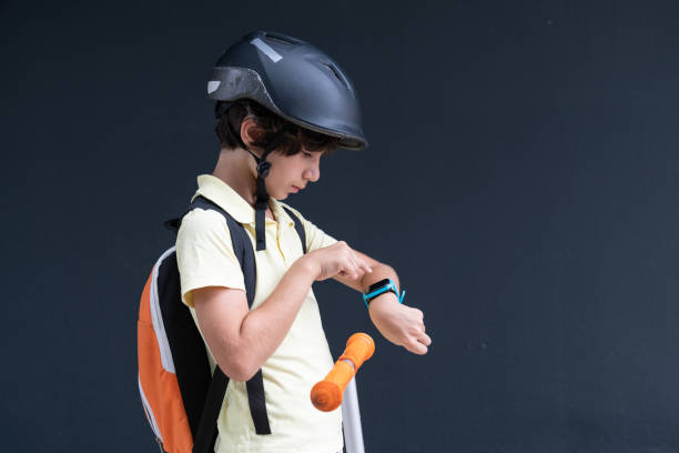 Photo Of Elementary Schoolboy Using Smart Watch While Riding Push Scooter In Outdoor
