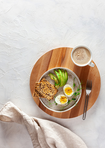 Plate with boiled eggs, avacado and crackers and a cup of coffee on the table