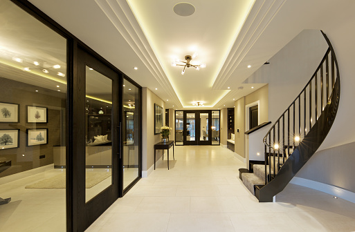 view from the front door towards the interior of a luxury home with a home-office on the left and staircase to the right. The ceiling features recessed light and cornice / coving.