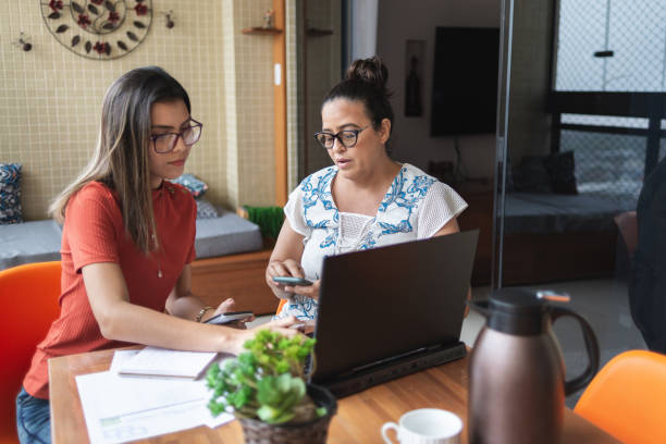 Mother and daughter doing finances together at home Mother and daughter doing finances together at home. They talk and handle some bills, looking and pointing at laptop screen college student and parent stock pictures, royalty-free photos & images