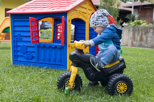 A little cute boy is playing in the yard with a children's motorcycle