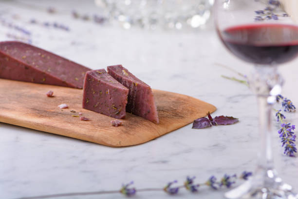 2 piezas de queso basiron lavanda sobre tabla de cortar de madera, flores de lavanda y copa de vino tinto sobre encimera de mármol blanco - basiron fotografías e imágenes de stock