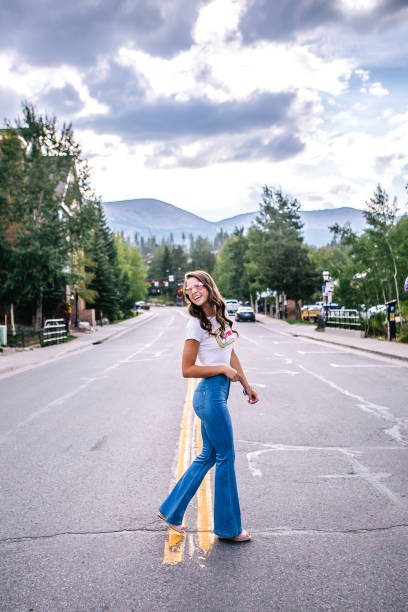 Full Length Portrait of a Beautiful, Fashionable Young Woman Wearing Flare Jeans and Sunglasses Walking Across the Street in a Colorado Mountain Town Full Length Portrait of a Beautiful, Fashionable Young Woman Walking Across the Street in Downtown Breckenridge, Colorado flare pants stock pictures, royalty-free photos & images