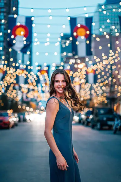 Portrait of a Beautiful, Fashionable Young Woman Standing Under Colorado Flags and String Lights on Larimer Square in Denver, Colorado at Dusk