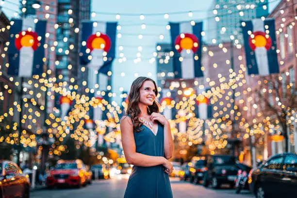 Portrait of a Beautiful, Fashionable Young Woman Standing Under Colorado Flags and String Lights on Larimer Square in Denver, Colorado at Dusk