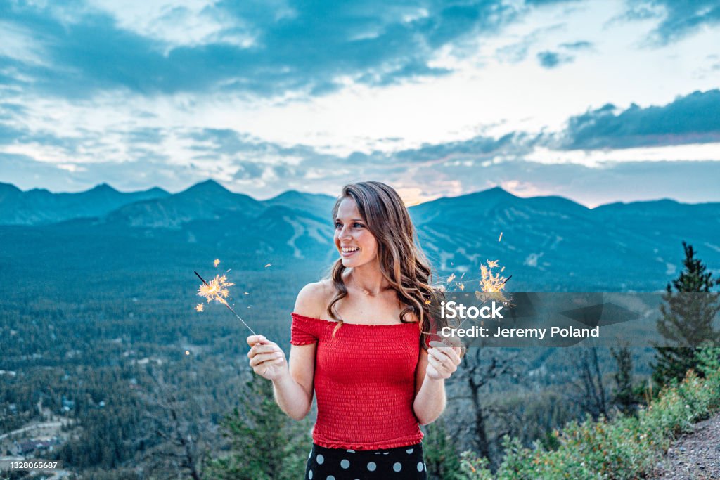 Artsy Dreamy Portrait of a Young Woman Standing Holding Sparkler Fireworks to Celebrate in the Summer With Beautiful Tenmile Range Mountain View in the Background Artsy Dreamy Portrait of a Young Woman Standing Holding Sparkler Fireworks to Celebrate in the Summer with a Beautiful Tenmile Range Mountain View of Quandary, Fletcher, Pacific, Crystal, and Peak 9 in the Background Breckenridge Stock Photo